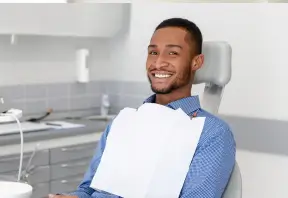 Smiling man sitting in a dental chair with a bib, in a dental office.