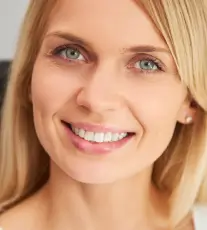 Close-up of a smiling blonde woman with green eyes and clear skin.