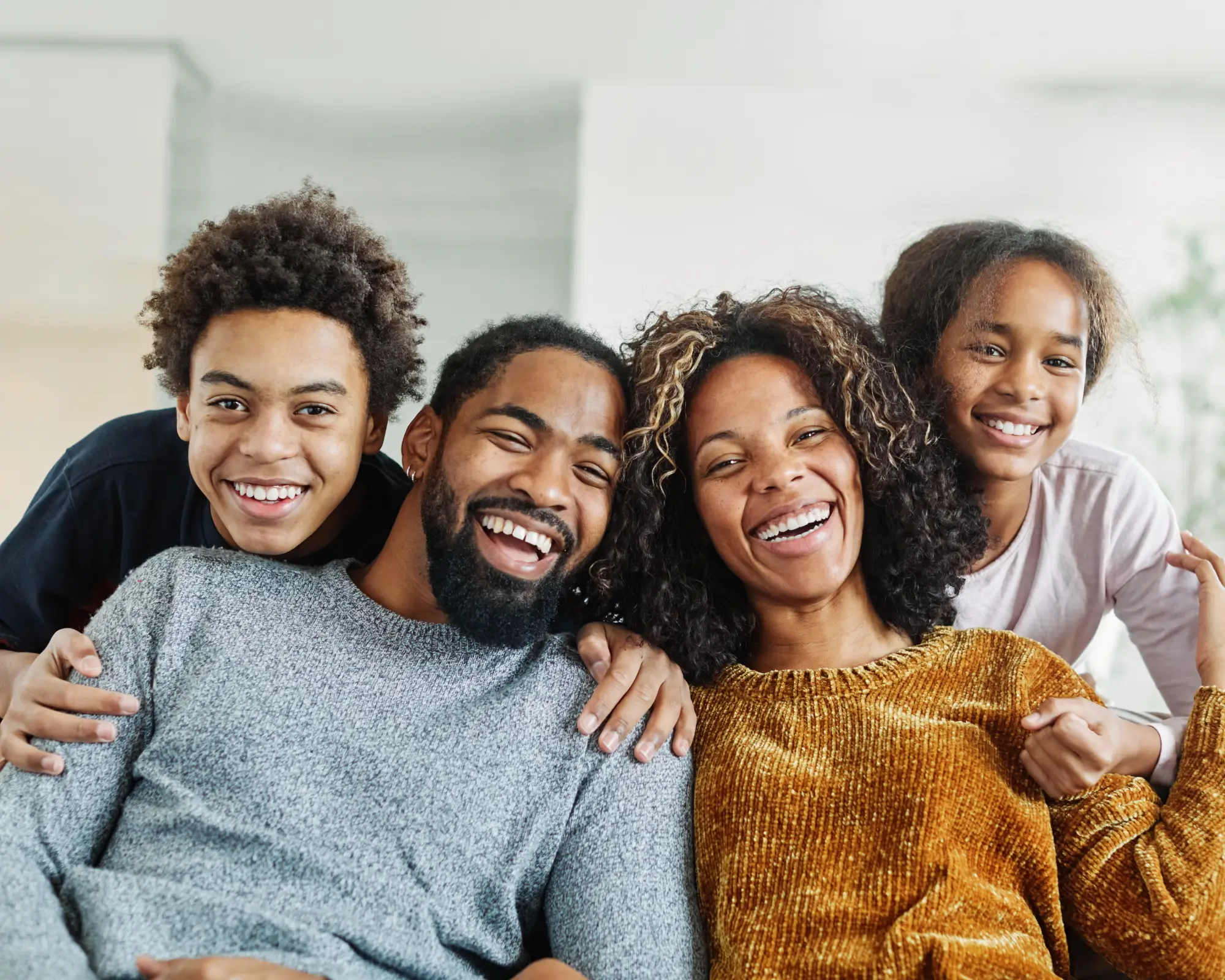 Smiling African American family of four sitting closely together indoors.