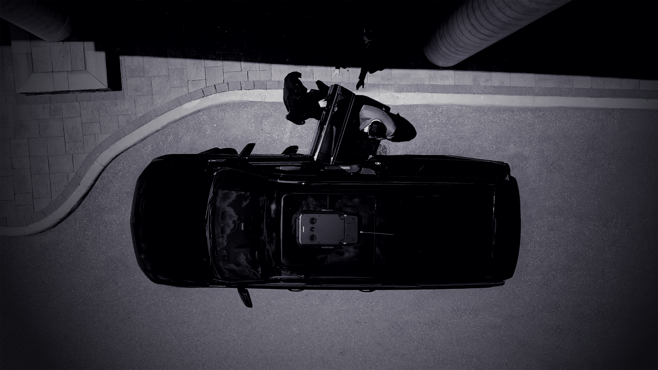 Top-down view of a black SUV stopped on a street curb with two people standing outside the open driver's door.