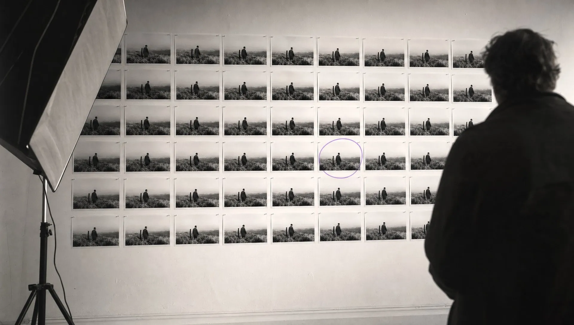 A person standing in front of a gallery wall of forty near-identical printed stills, one circled in violet