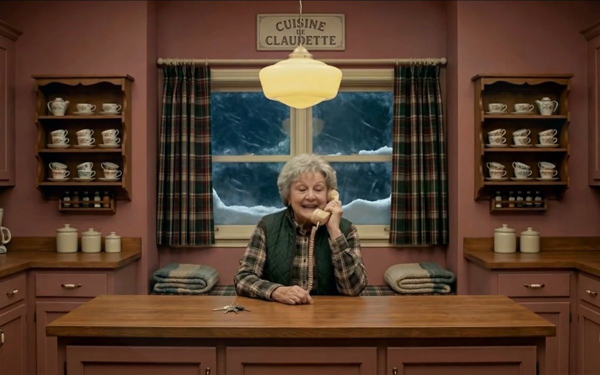 A frame from the AccèsPharma film: a pharmacist on the telephone in a warm, symmetrical kitchen set under a hanging lamp