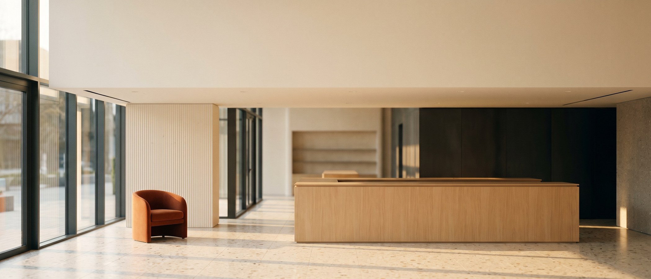 A calm, empty modern retail interior with a light oak service counter, terrazzo floor, and warm afternoon light through tall windows.
