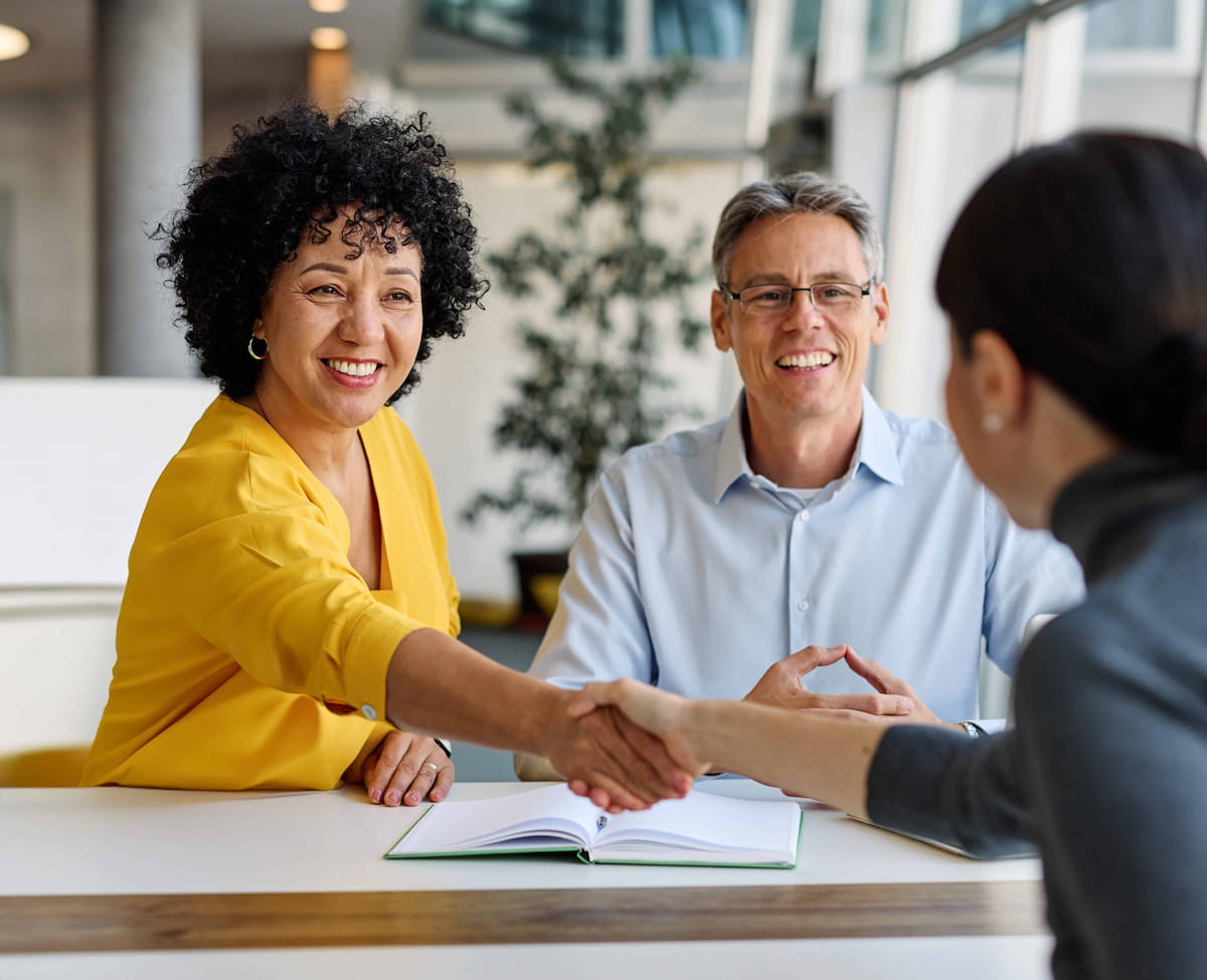 Two people shaking hands across a table during a professional financial meeting.