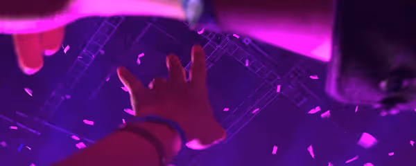 Hand reaching up towards stage lights and falling confetti against a dark purple-lit background.