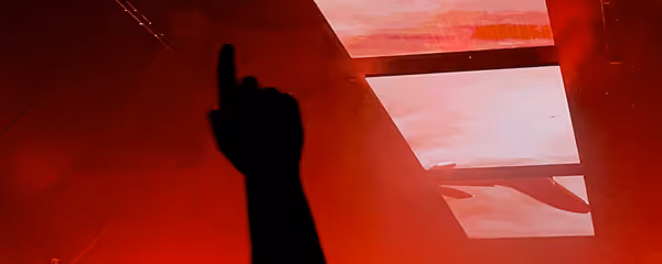 Silhouette of a raised hand pointing upwards against a red background with two illuminated rectangular panels.