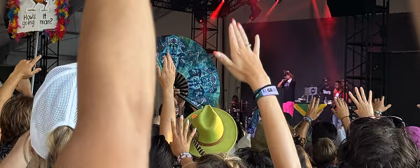 Crow with raised hands watching a live performance on stage with singers under red and purple lights.