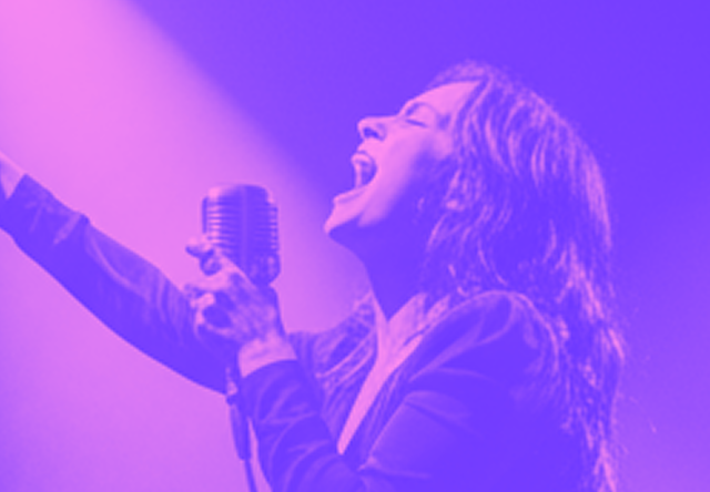 Woman passionately singing on stage holding a vintage microphone with one arm raised.