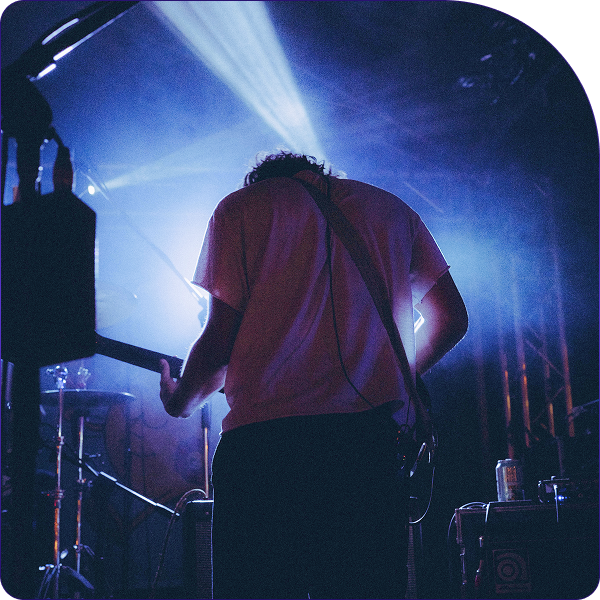 Musician playing electric guitar on stage with blue spotlight and fog effects behind them.