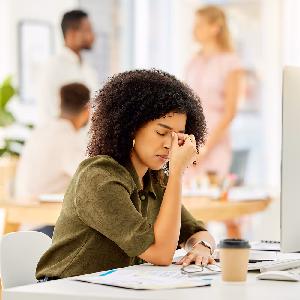 A young professional woman at a desk showing signs of work-related exhaustion, seeking burnout and career stress therapy at Ray of Hope Counseling in Texas.