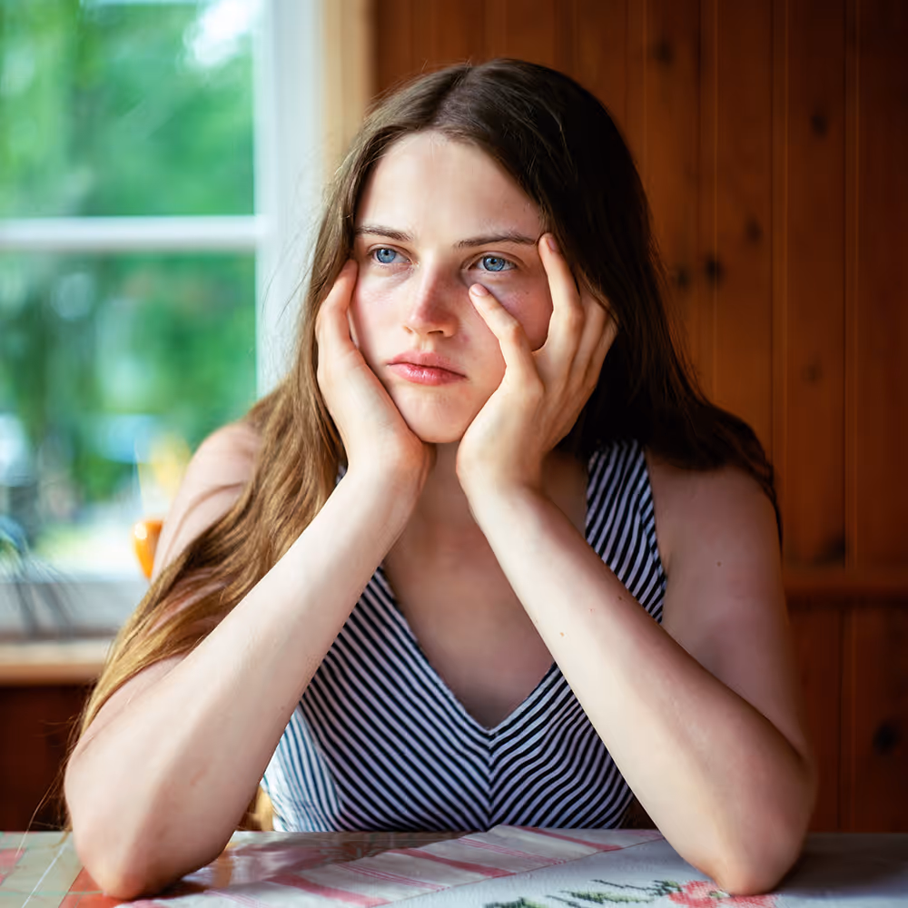 A young woman looking pensive and tired from the pressure of perfectionism, seeking support through online therapy at Ray of Hope Counseling in Texas.