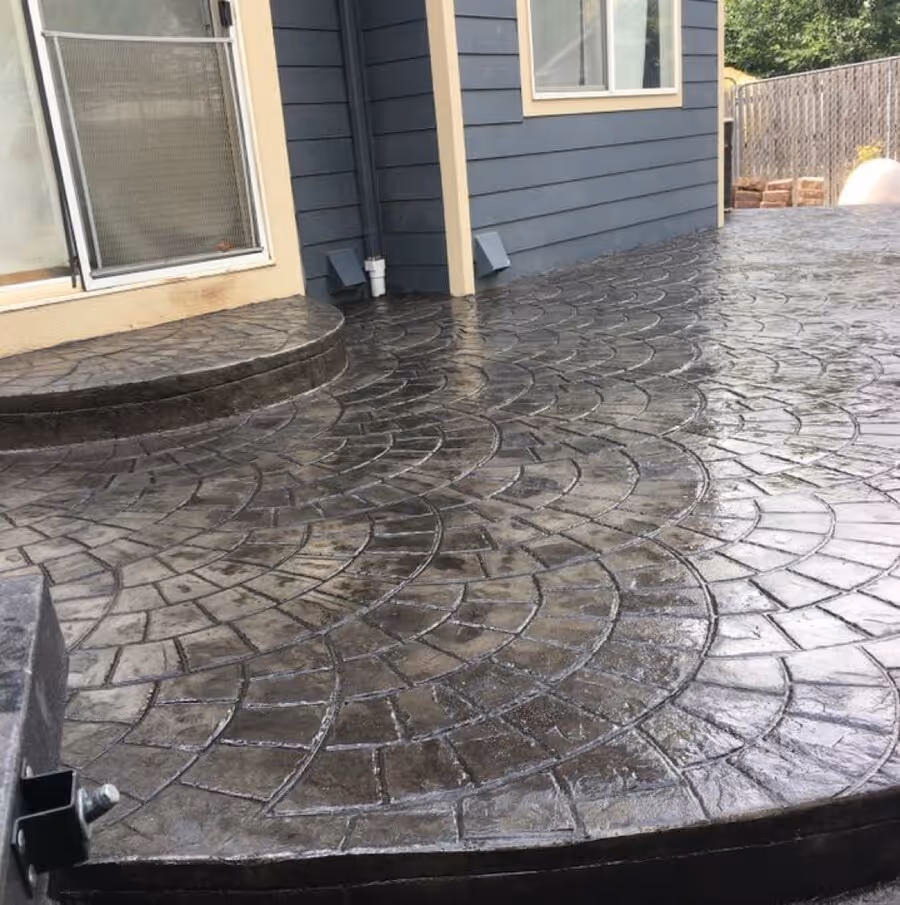 Wet stamped concrete patio with a semi-circular step next to a blue house exterior.