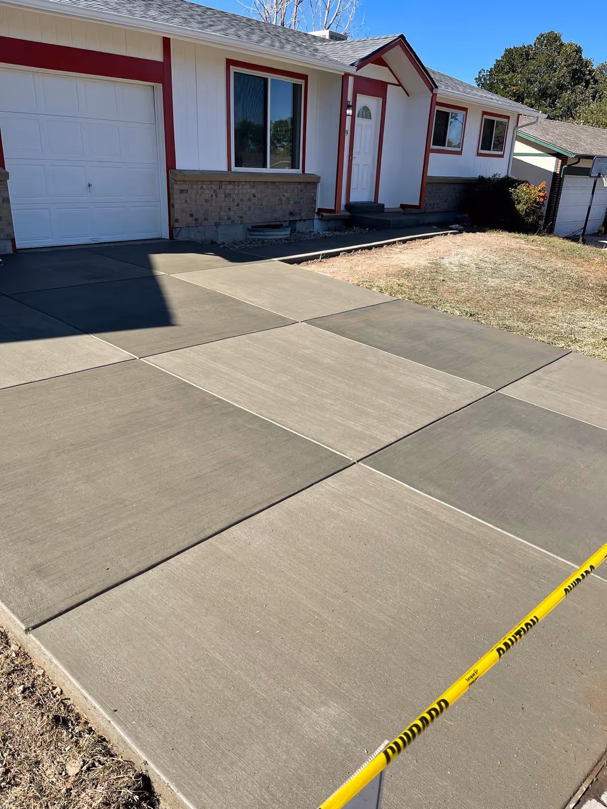 Newly poured concrete driveway in front of a house with yellow caution tape across the bottom right corner.