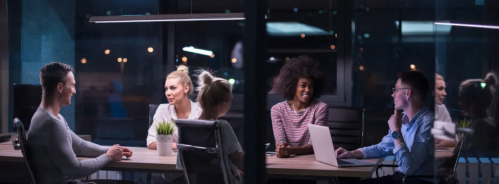 Five colleagues having a discussion around a table in a modern office at night.