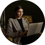 Woman in a gray blazer working on a laptop in a dimly lit room.