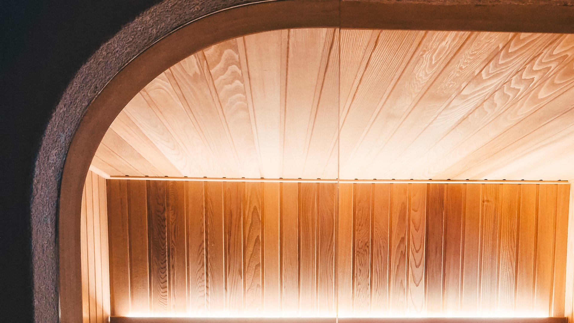 A traditional Western Red Cedar sauna behind a curved bronze-glass archway, built into a small under-house wellness retreat in Bellevue Hill.