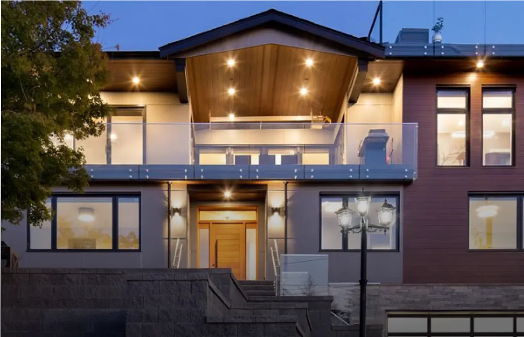 Modern two-story house exterior at dusk with warm interior lights and outdoor balcony.