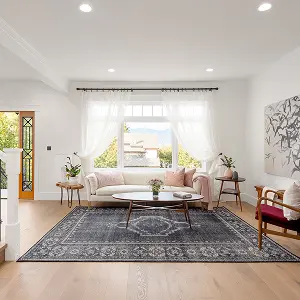 Bright living room with large window, white sheer curtains, light pink sofa, wooden coffee table, patterned gray rug, and cozy armchair.