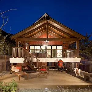 Wooden cabin with a lit porch and outdoor seating under a clear night sky.