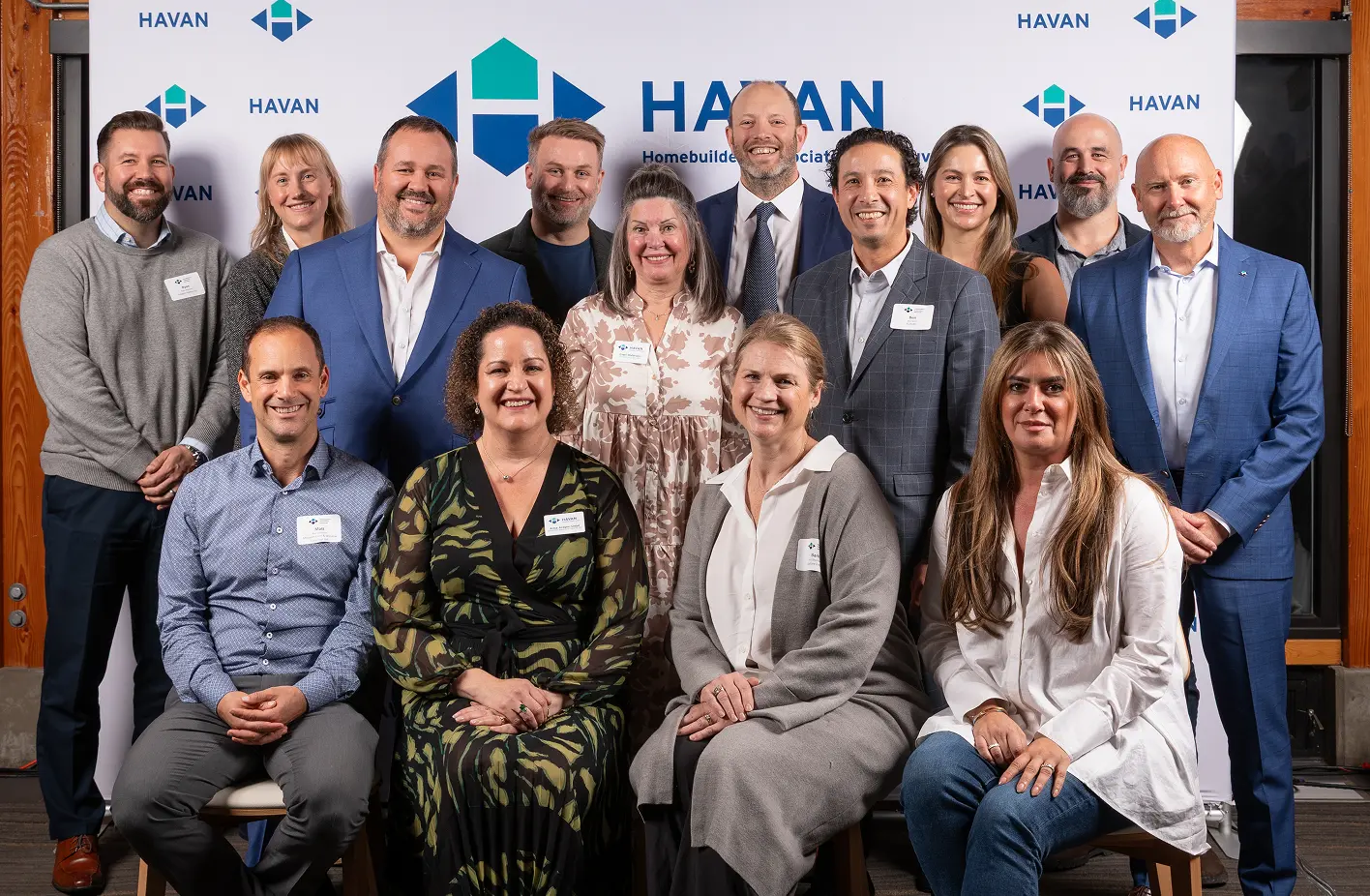 Group of fourteen professionally dressed people posing and smiling in front of a HAVAN Homebuilders Association backdrop.