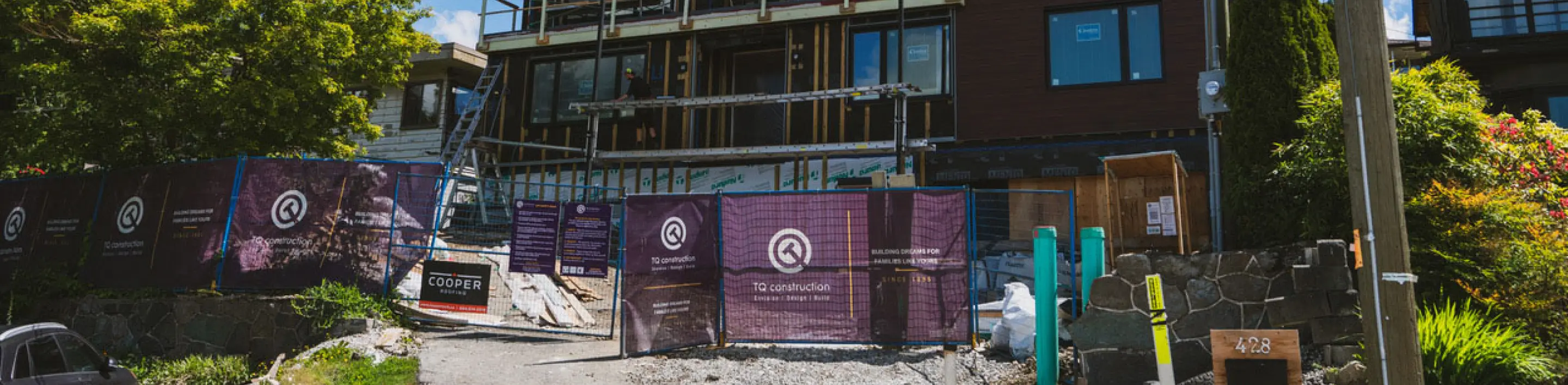 Construction site of a building with purple TQ Construction fencing and workers installing windows.