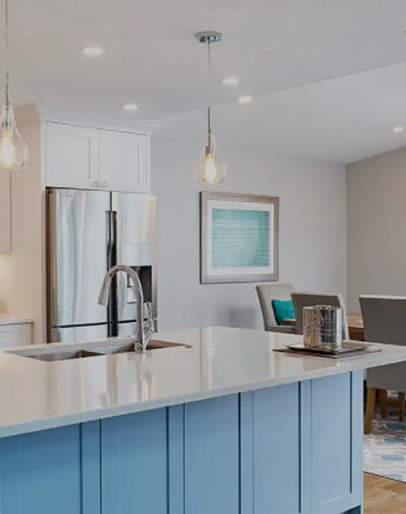 Modern kitchen with a blue island, white countertop, stainless steel refrigerator, and a framed artwork on the wall.