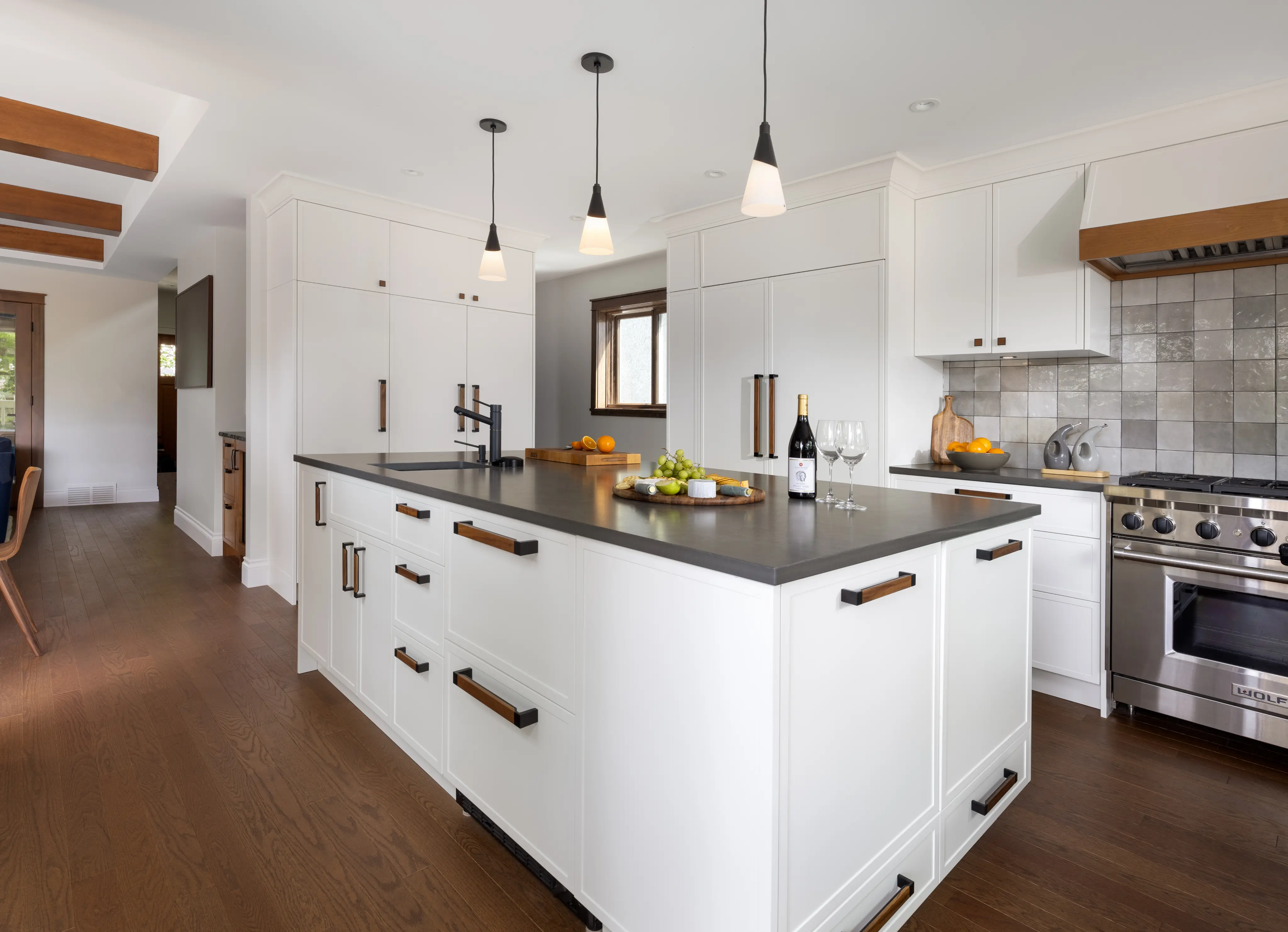 Modern kitchen with white cabinetry, a large island with dark countertop, stainless steel stove, and three pendant lights.