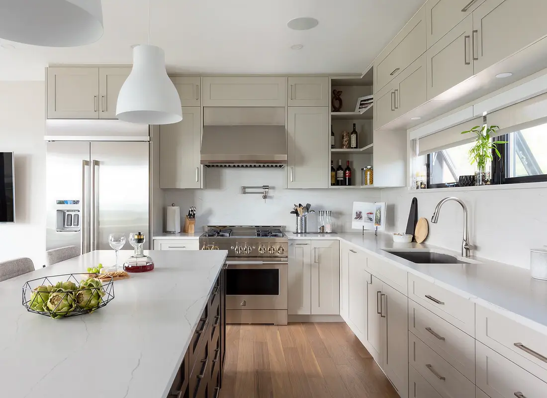 Modern kitchen with white cabinetry, stainless steel appliances, marble countertop island, and wooden floor.