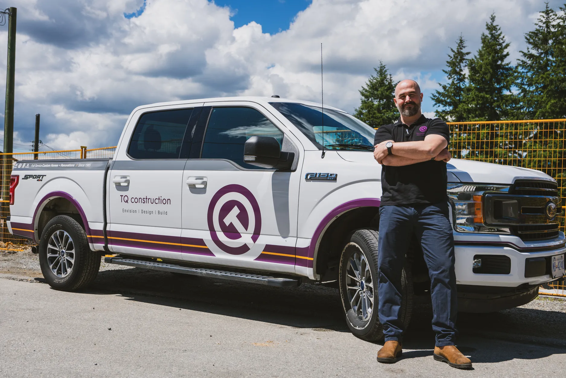 Man with crossed arms standing next to a white pickup truck branded with TQ Construction logo and text.