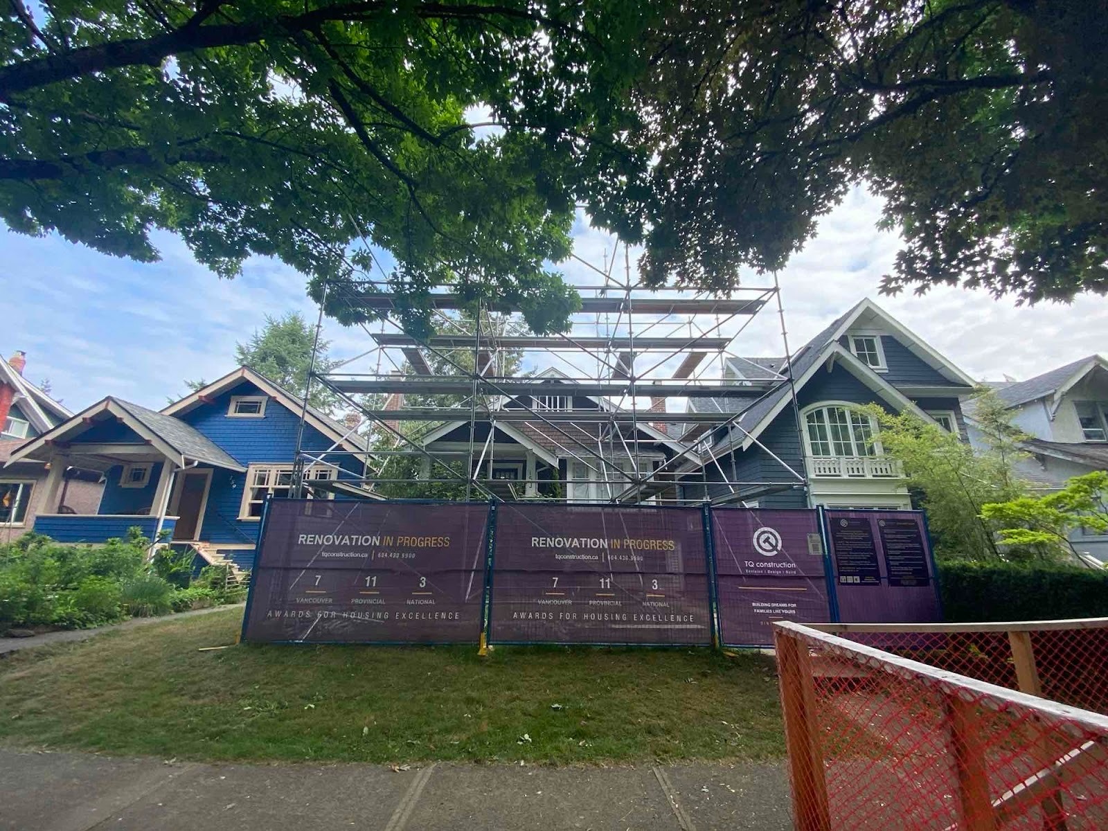 Exterior of a two-storey home under renovation with scaffolding and a small crew reviewing plans