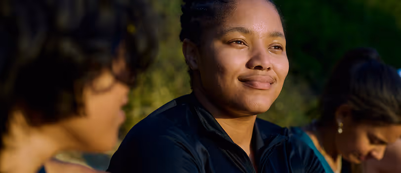 Close-up of a woman smiling outdoors with blurred people in the background.