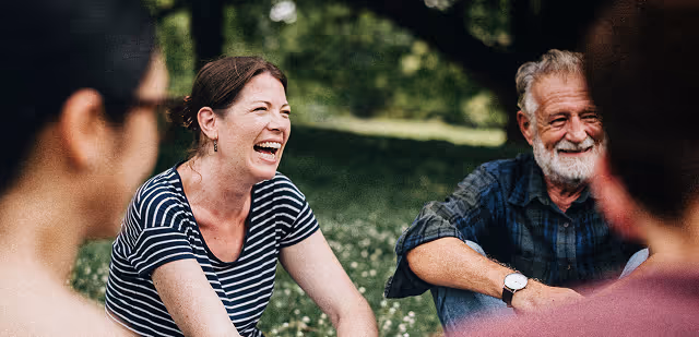 Group of people sitting outdoors on grass, laughing and enjoying a conversation.
