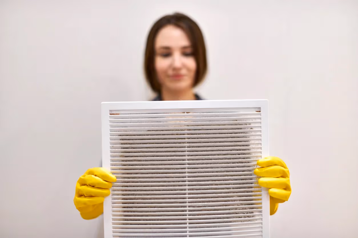 A person wearing yellow gloves holds a clean pleated air filter