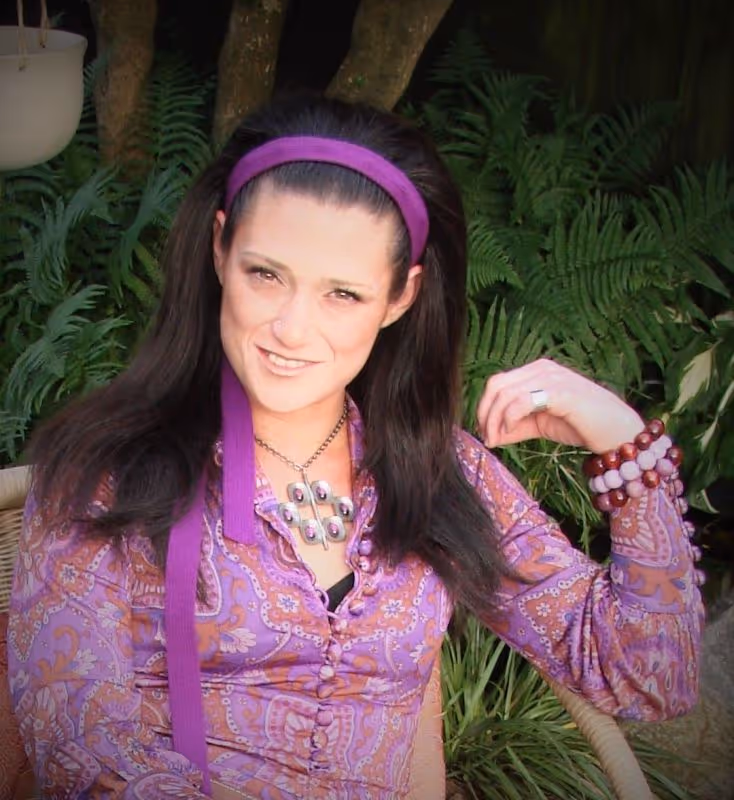 Smiling middle-aged man with short hair and salt-and-pepper beard wearing a light blue button-up shirt outdoors.