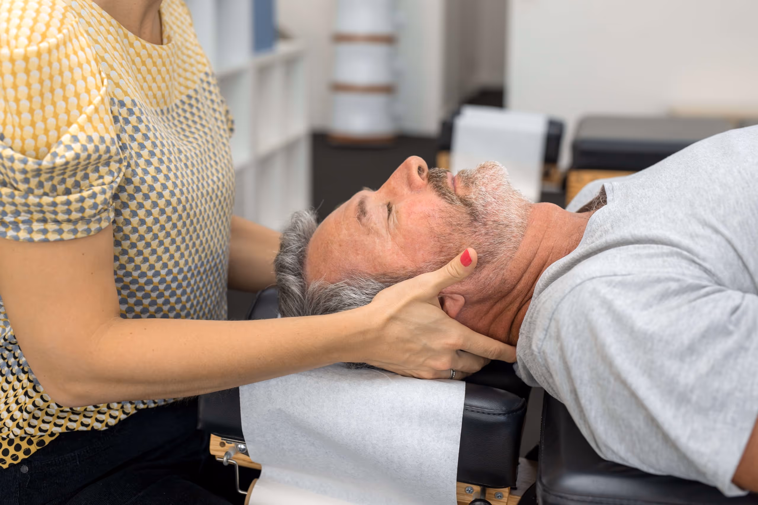 Therapist gently holding an older man's head during a chiropractic or physical therapy session.
