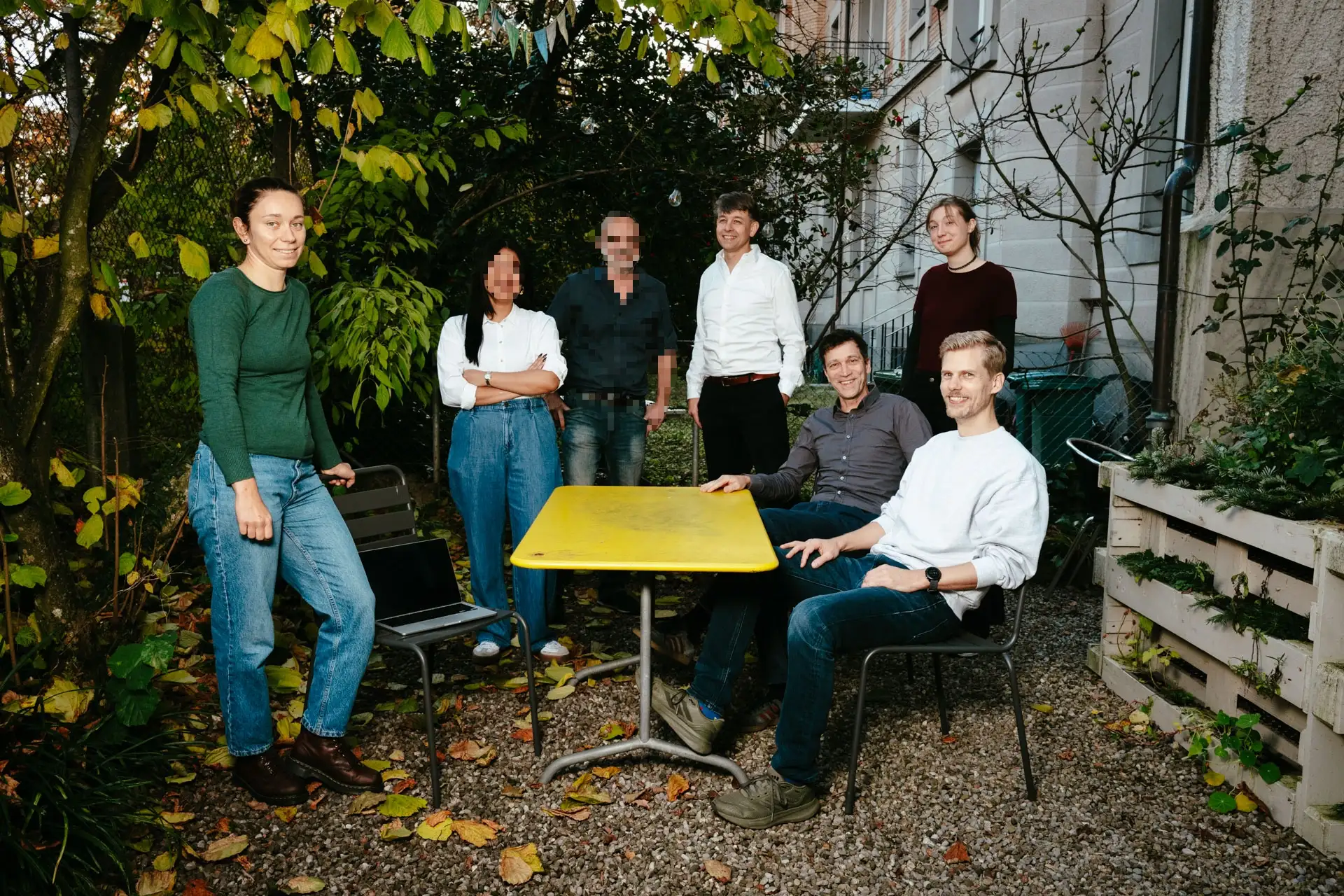 Gruppenfoto eines Teils der Belegschaft von STURM UND BRÄM. Die Personen sitzen und stehen draussen um einen gelben Gartentisch.