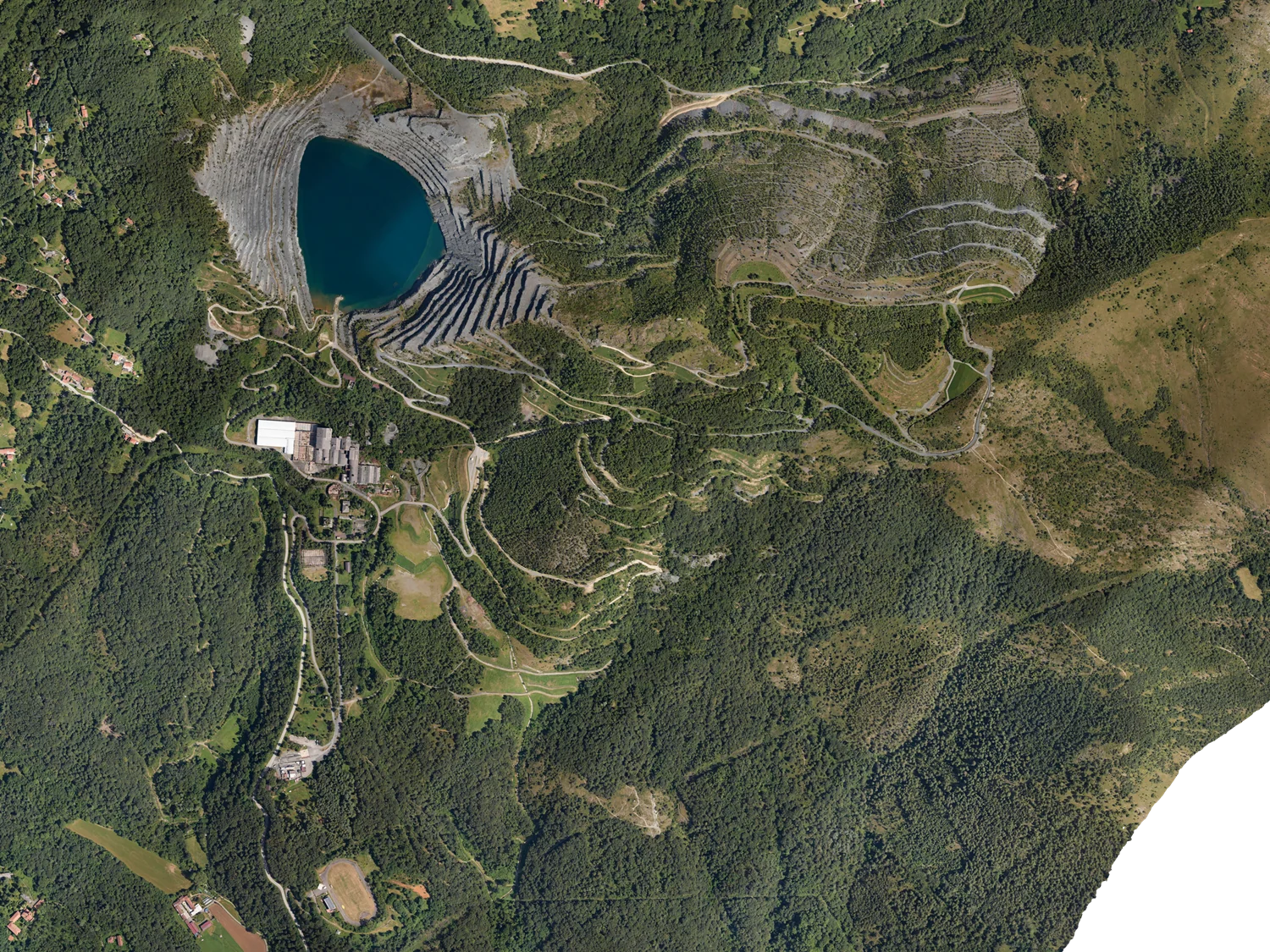 Veduta dell’interro sito minerario con lago blu intenso, pareti rocciose, boschi fitti e viabilià