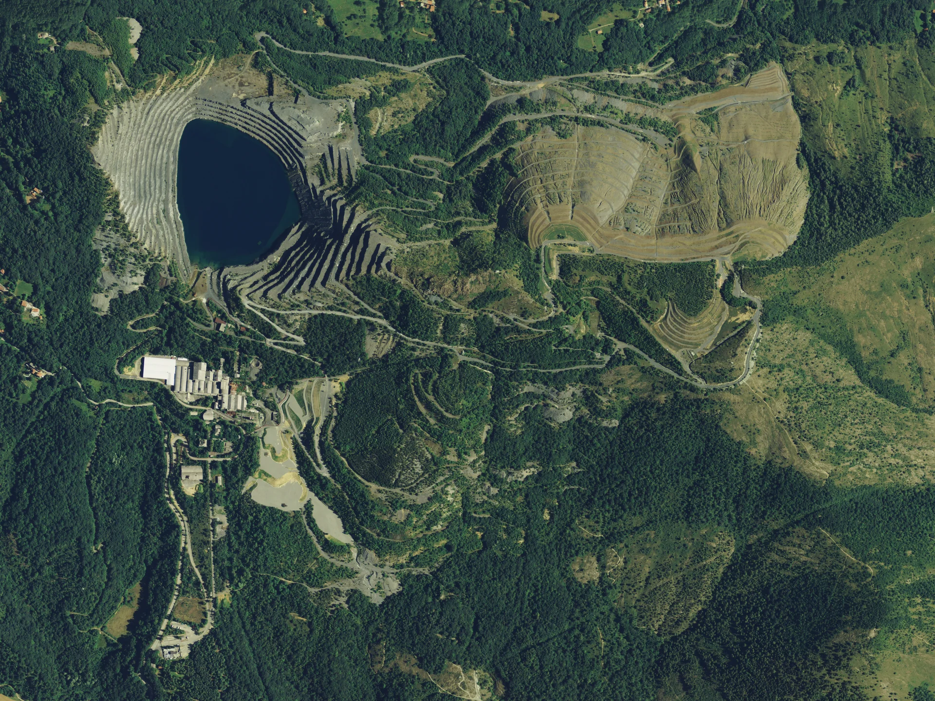 Veduta dell’interro sito minerario con lago blu intenso, pareti rocciose, boschi fitti e viabilià