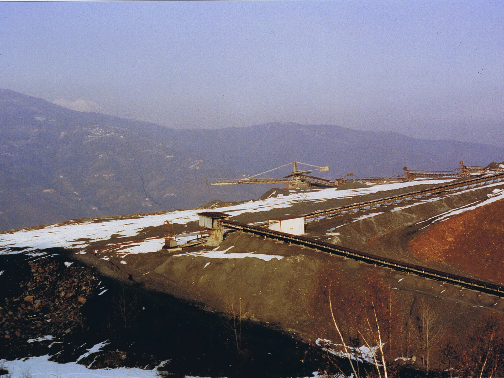 Industrial conveyor belts on a snowy hillside with mountain range in the background.