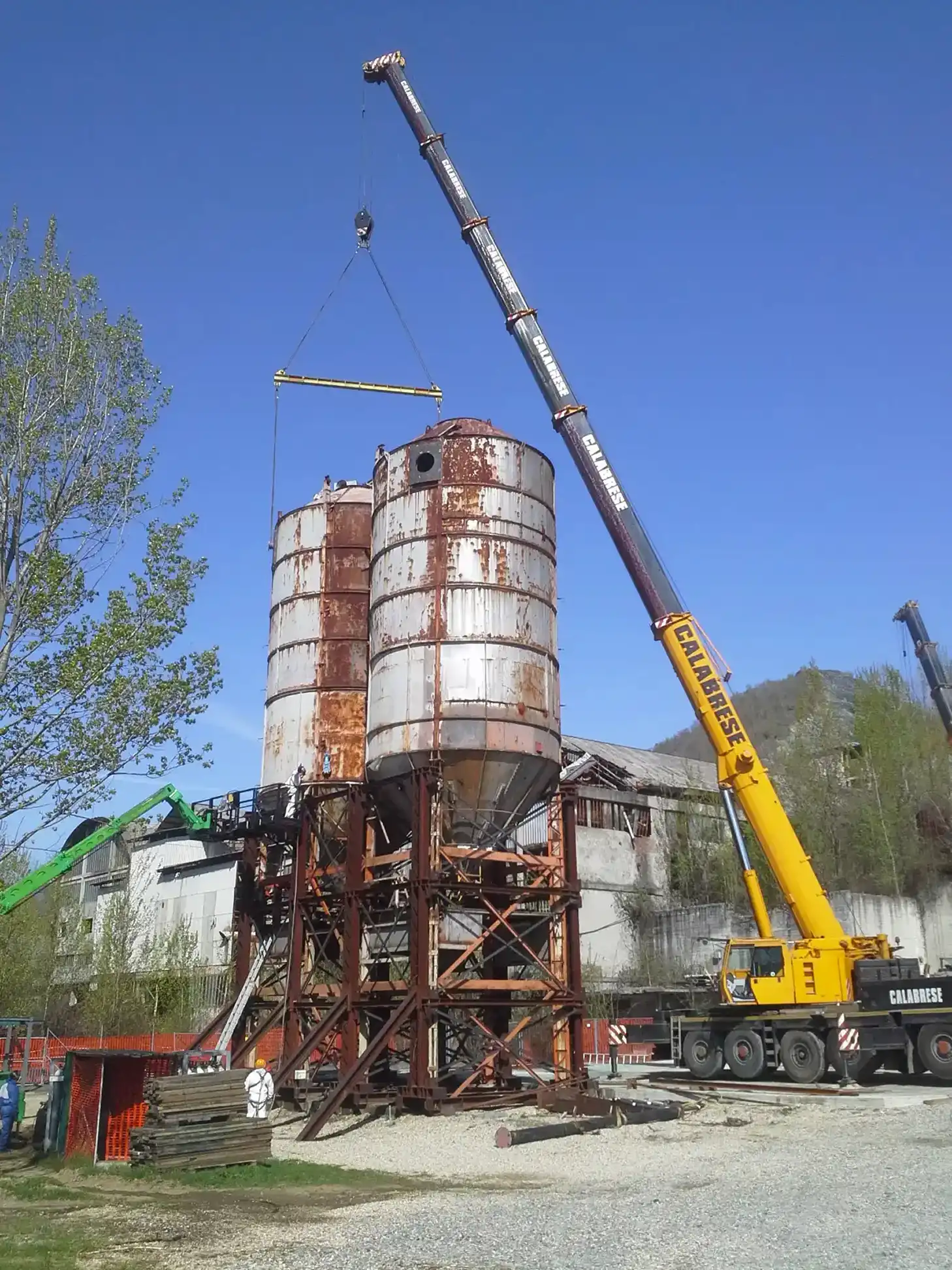 Pinza idraulica gialla che taglia rottami metallici e travi arrugginite in un cantiere di demolizione