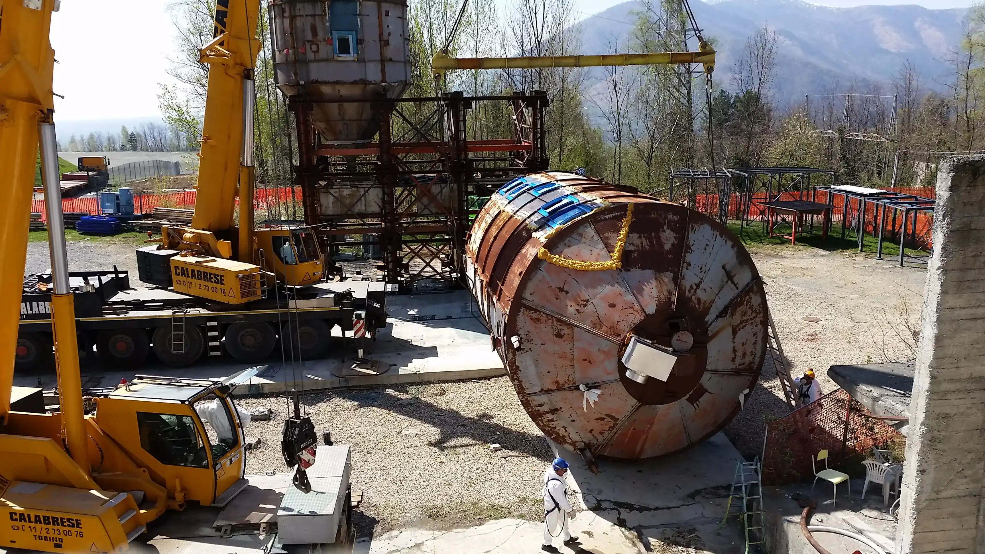 Escavatore a braccio lungo solleva rottami della demolizione dell’edificio metallico sotto acqua nebulizzata per contenere le polveri