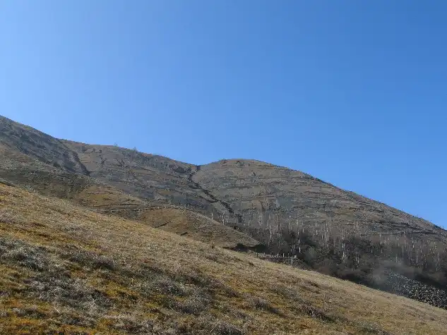 Ampio versante della discarica lapidea lato Corio con pendenze accentuate sotto un cielo terso con copertura erbacea