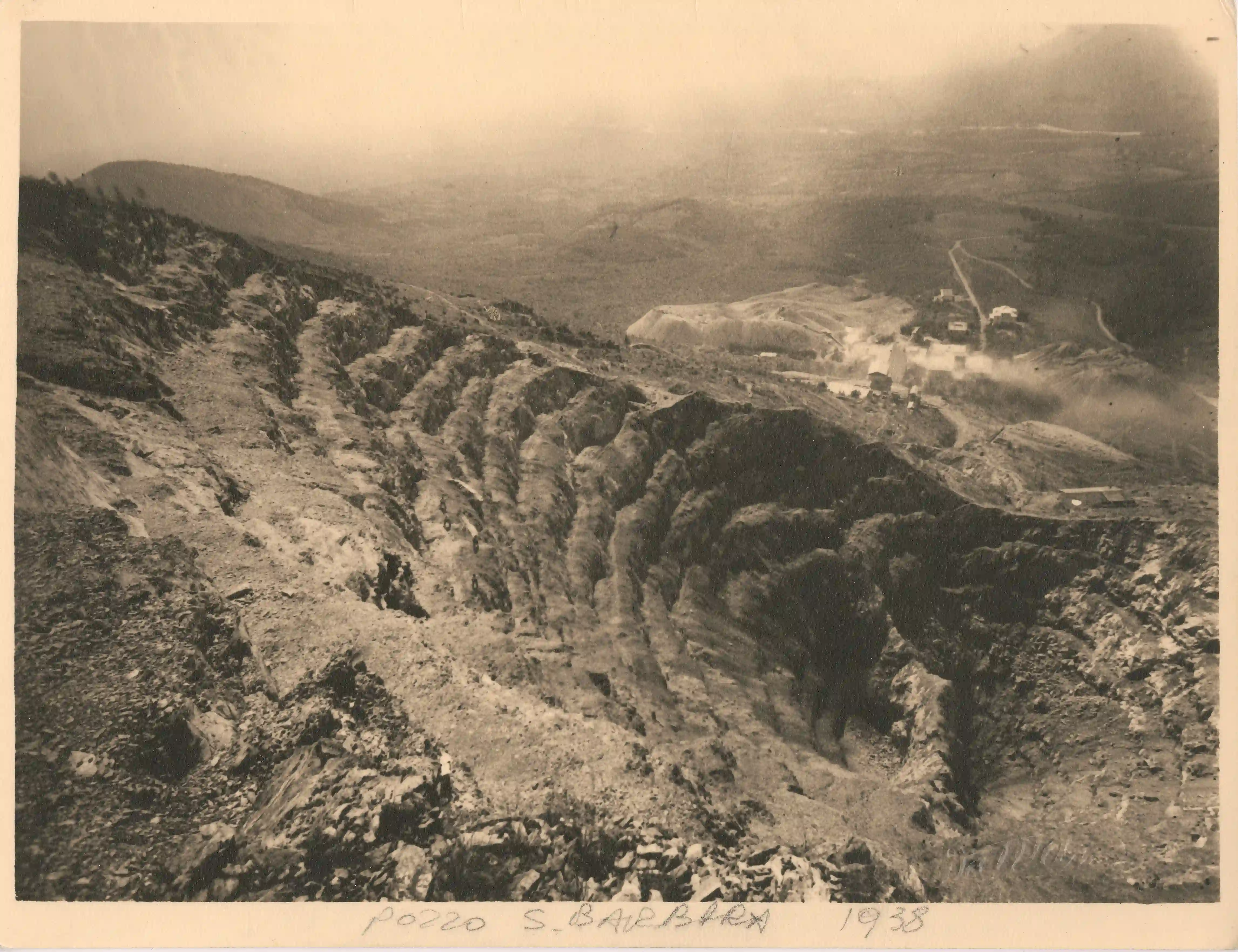 Veduta dall'alto dei profondi gradoni del Pozzo S. Barbara nel 1938, con impianti industriali a valle e vista della pianura della Stura