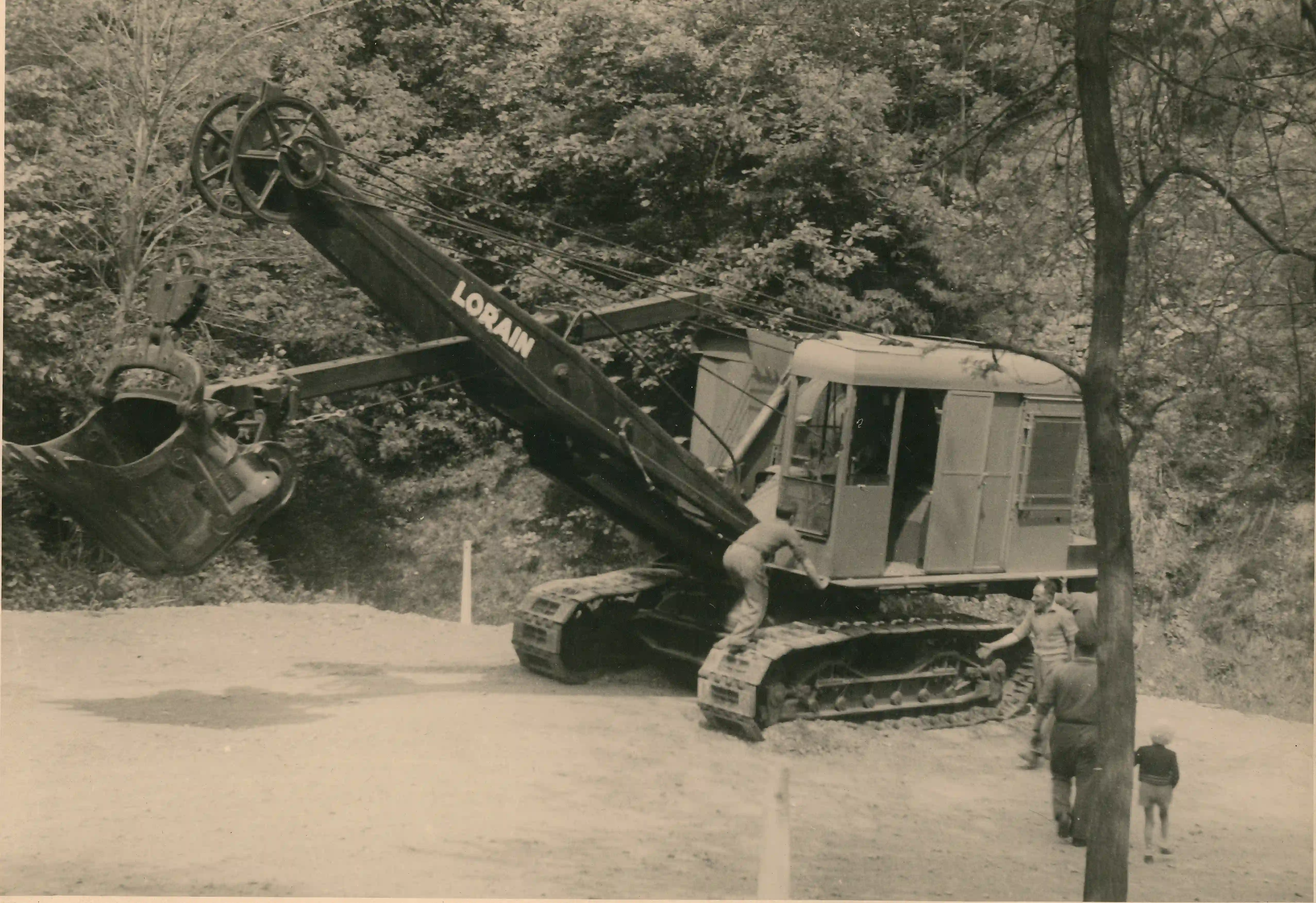 Escavatore meccanico d'epoca marca Lorain su una strada sterrata tra gli alberi, con persone accanto al mezzo