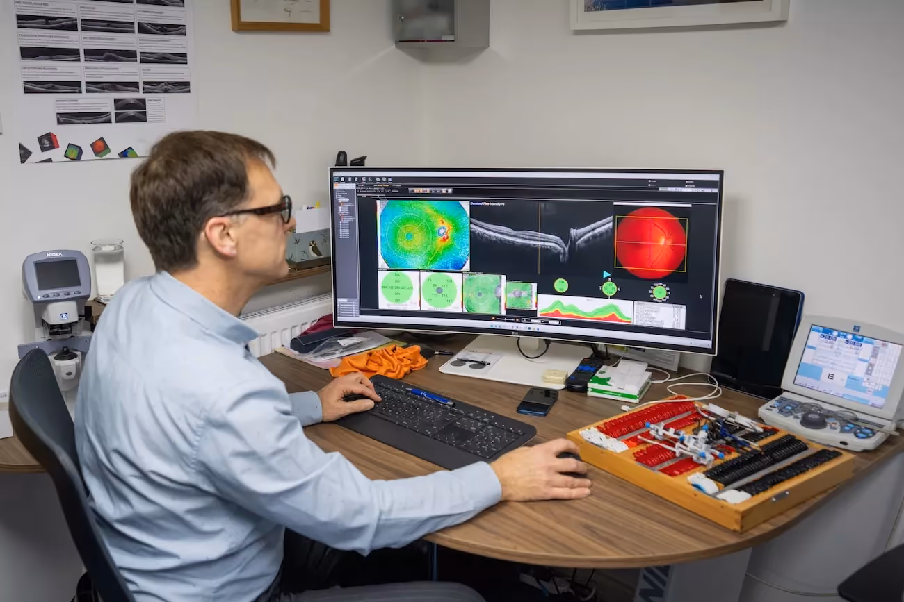 Optometrist analysing OCT retinal scan and corneal topography results on screen