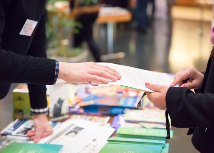 Hände die eine Broschüre entgegennehmen