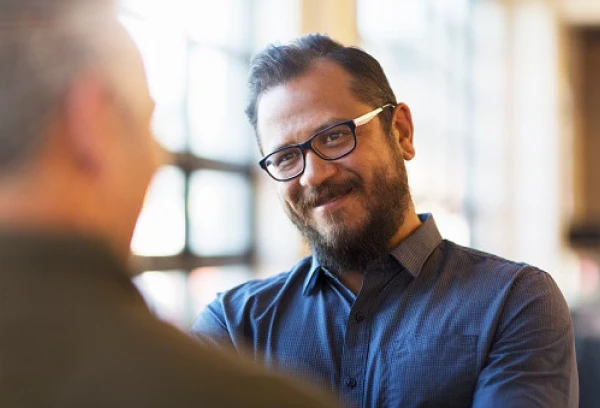 Smiling man with glasses and beard engaged in a conversation in a bright office setting.