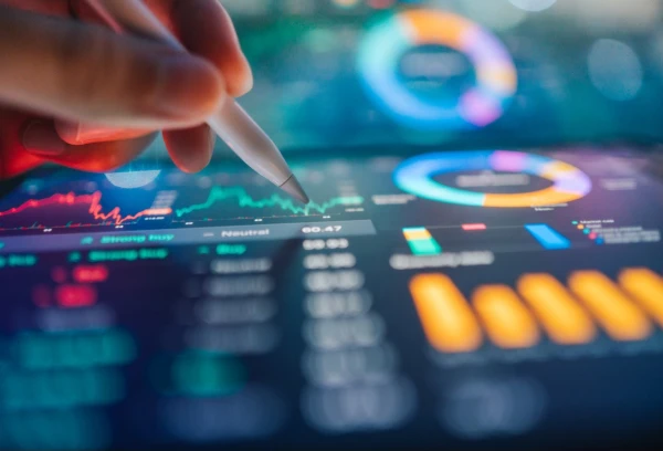 Hand holding stylus pointing at a digital touchscreen showing colorful financial charts and data analytics dashboards.
