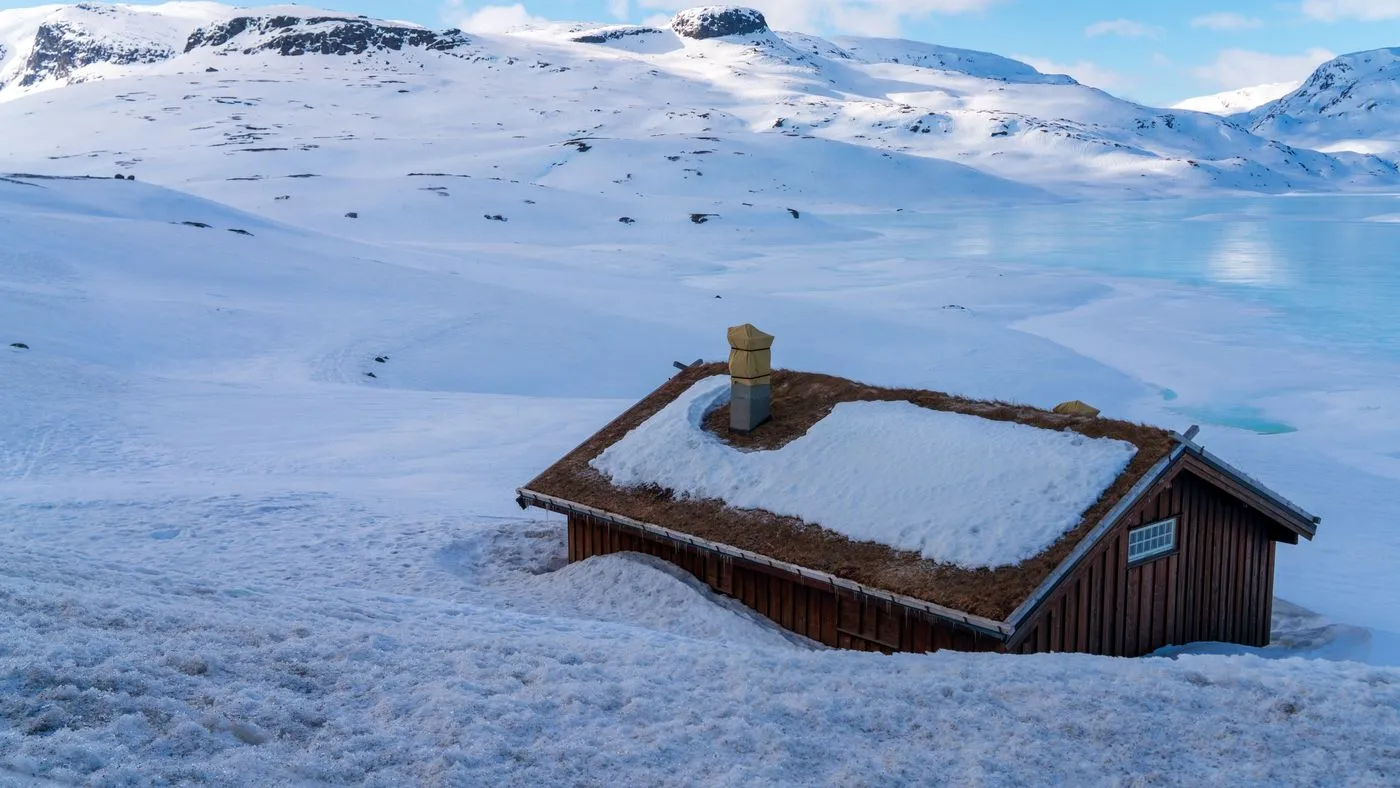 Snødekt hytte med fjell i bakgrunnen.