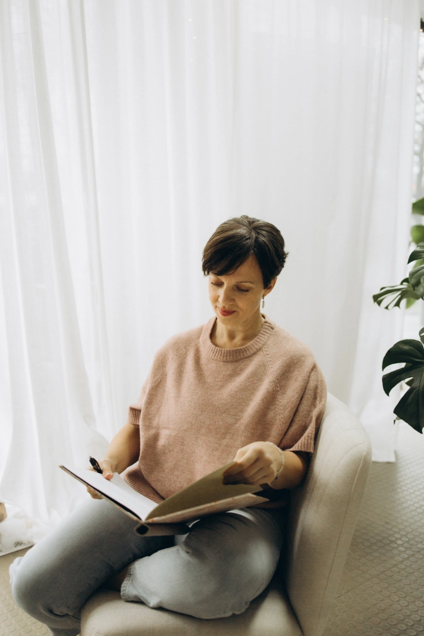 Anna Fasciani - freie Traurednerin -  in rosa Pullover sitzt auf einem Stuhl und liest in einem Buch mit einem Stift in der Hand.